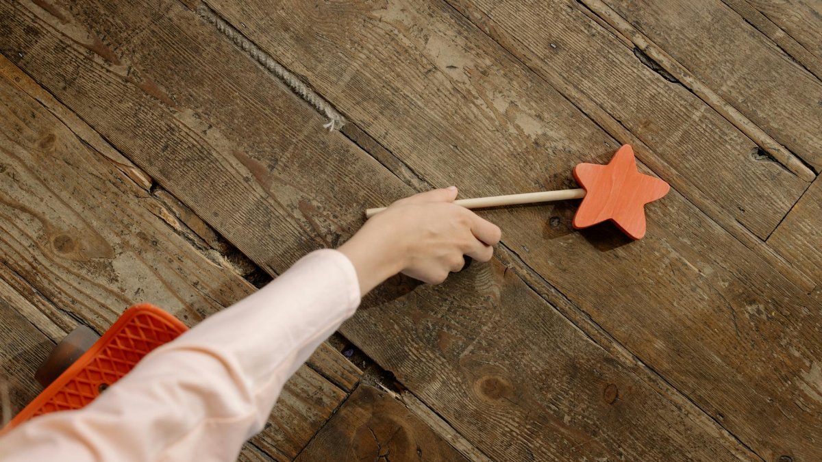 Close-up of a child's hand holding a star-shaped wand on rustic wooden flooring, from above.