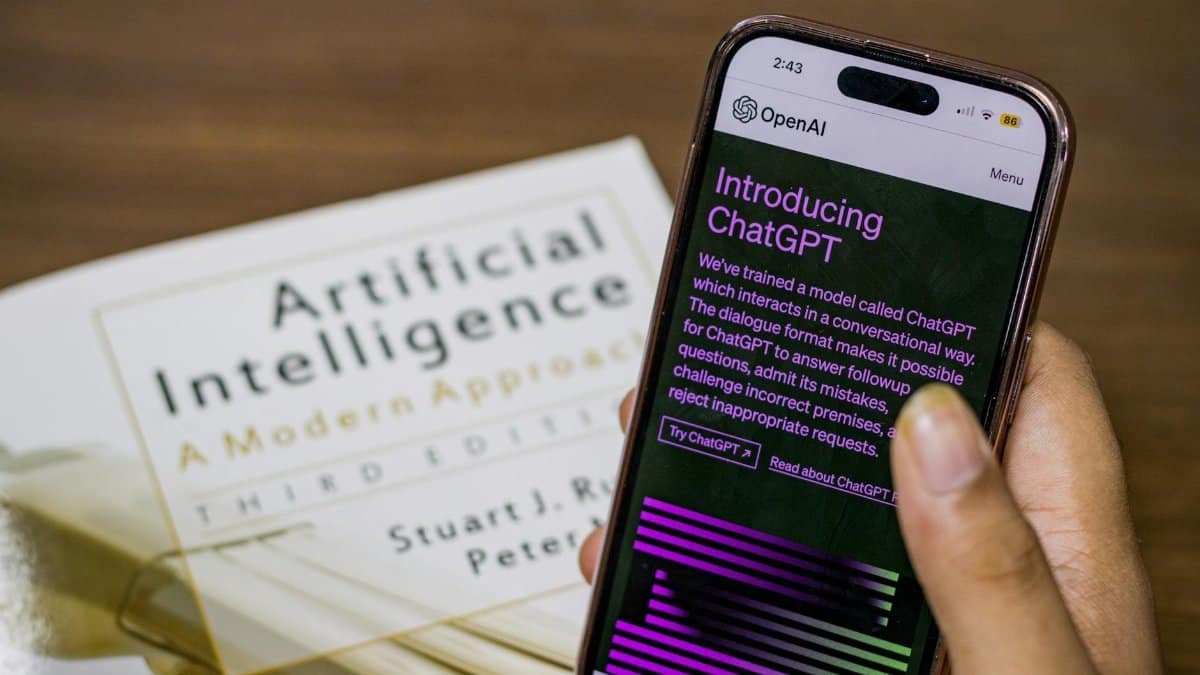 Close-up of a smartphone displaying ChatGPT app held over AI textbook.
