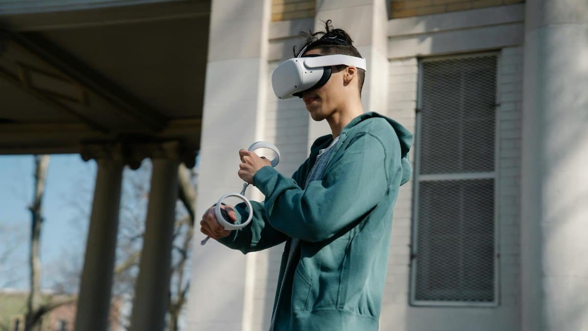 A young man wearing a VR headset and controllers stands in an urban outdoor setting, enjoying virtual reality.