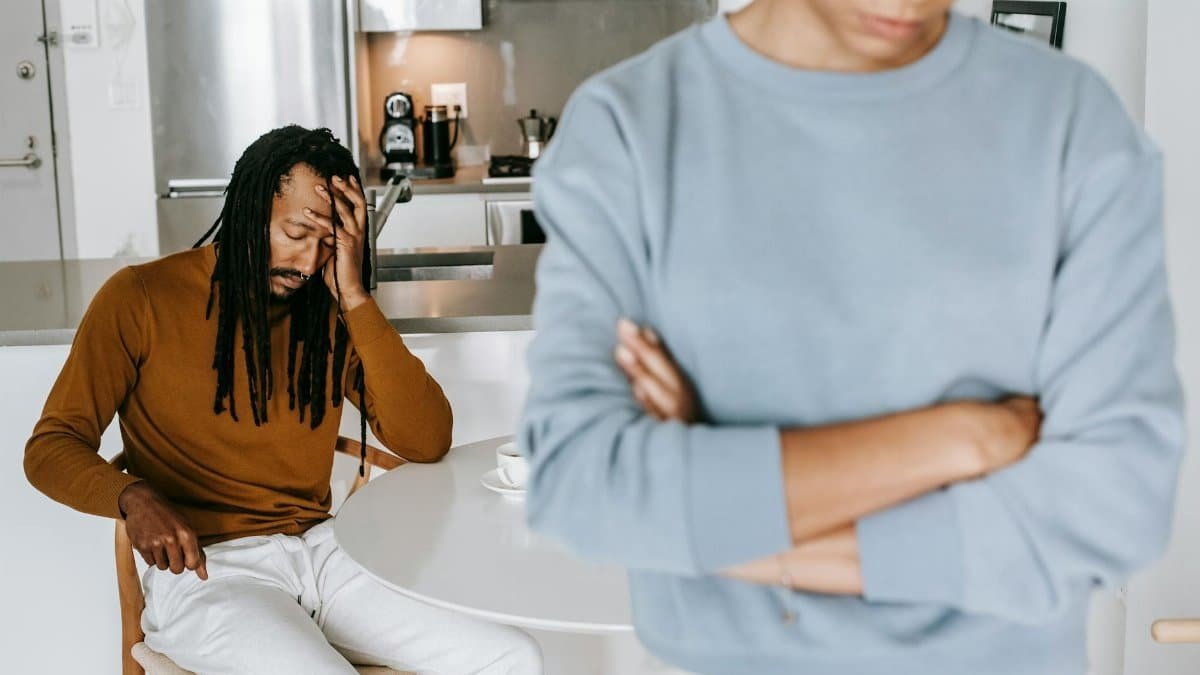A couple faces relationship issues at home, appearing stressed and distant in a kitchen setting.