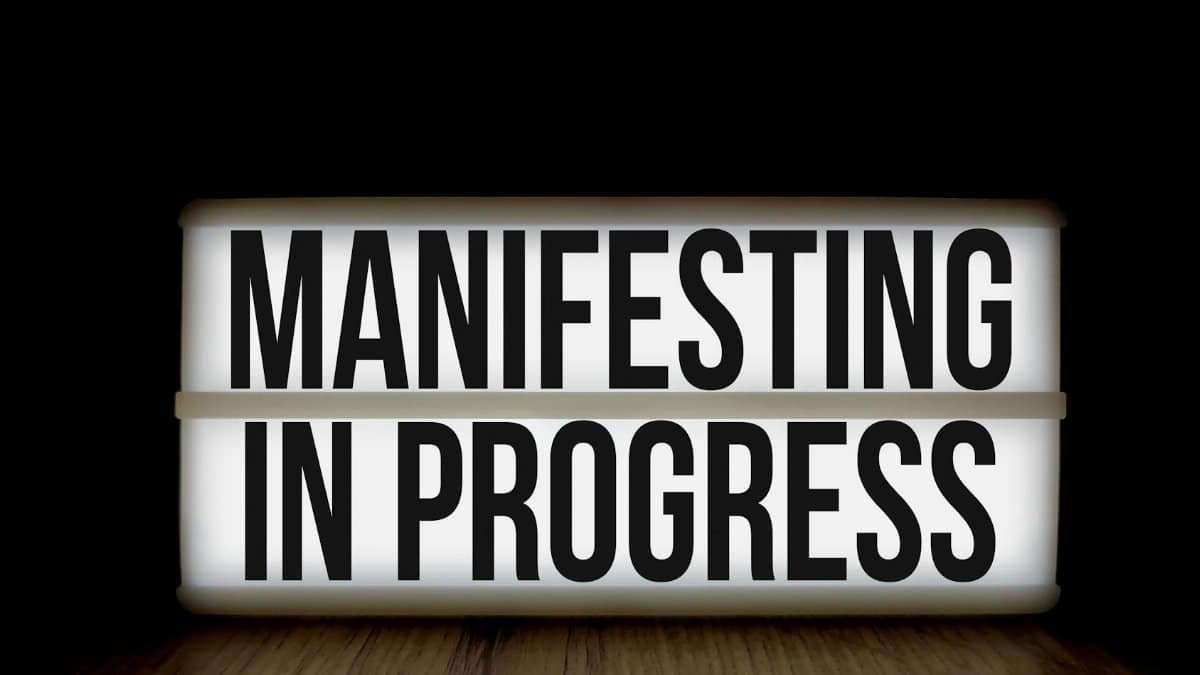 Illuminated lightbox sign with the motivational message 'Manifesting in Progress'.