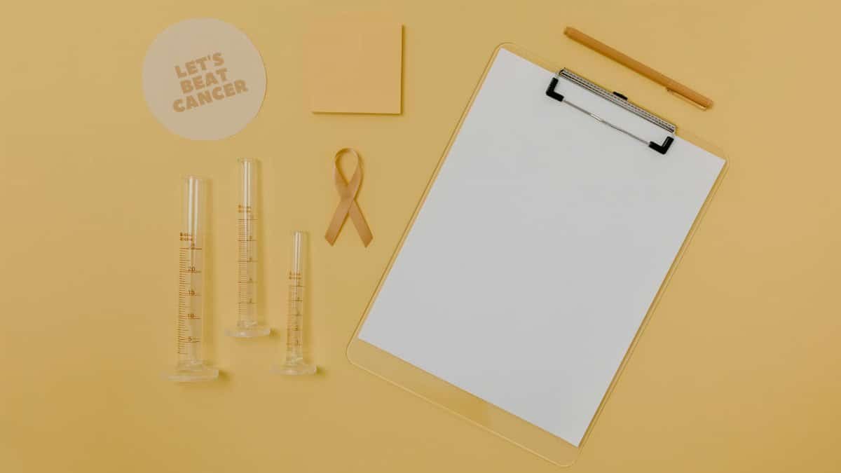 Flat lay of medical tools and cancer awareness ribbon on yellow background.