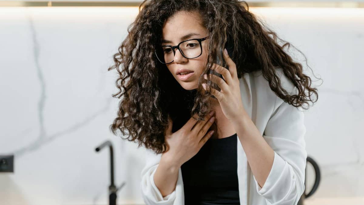 Young woman with curly hair making an urgent phone call indoors, looking concerned.