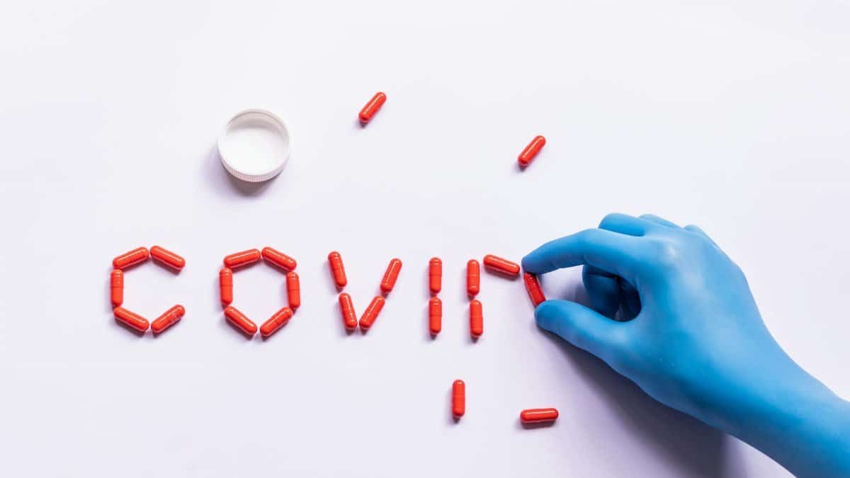 Top view of crop unrecognizable doctor in latex glove making word COVID with capsules for treating viral disease on white background