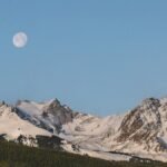 Stunning view of snow-covered mountains under a full moon in Colorado's winter landscape.