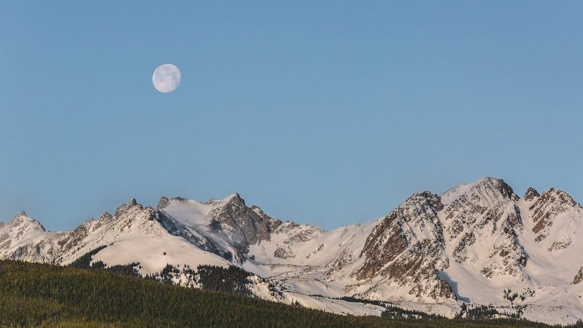 Stunning view of snow-covered mountains under a full moon in Colorado's winter landscape.