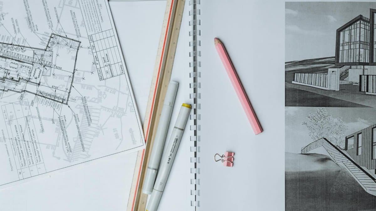 Flat lay of architectural blueprints, drawing tools, and stationery on a desk surface.