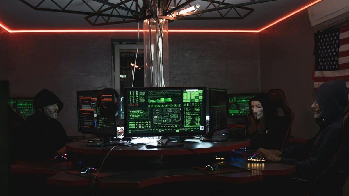 Team of hackers with Guy Fawkes masks coding in a dark room with computers.