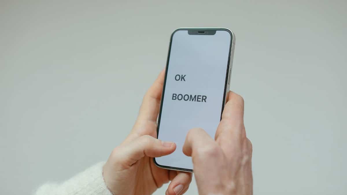 Close-up of a person holding a smartphone displaying 'OK Boomer' against a plain background.