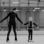 A mother teaching her daughter figure skating in an indoor ice arena.