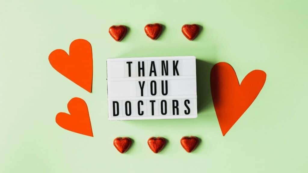 Top view of red heart shaped decorative elements and white retro light box with THANK YOU DOCTORS gratitude message arranged on green background