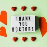 Top view of red heart shaped decorative elements and white retro light box with THANK YOU DOCTORS gratitude message arranged on green background