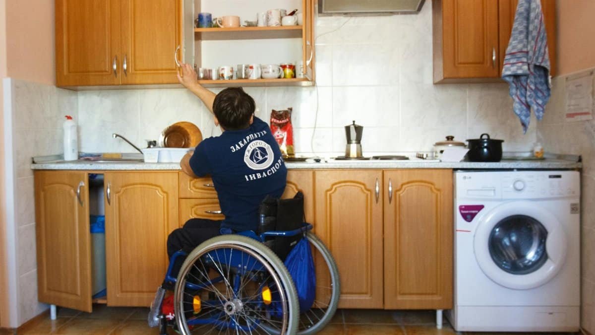 An individual in a wheelchair reaching for a kitchen shelf, demonstrating accessibility.