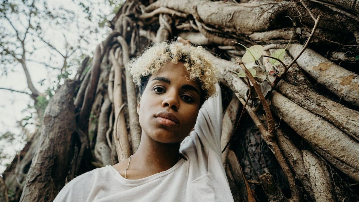 Young woman with curly hair posing against tree roots in a jungle setting.