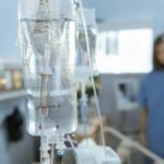 Close-up of an IV drip in a hospital with a blurred nurse in the background.