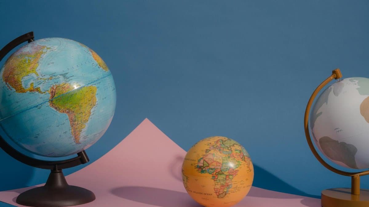 Three vividly colored globes displayed against a blue and pink backdrop, highlighting geography and education.