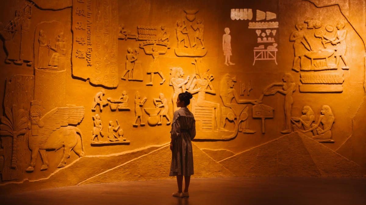 Back view of anonymous female traveler standing near ancient wall with Egyptian engraving