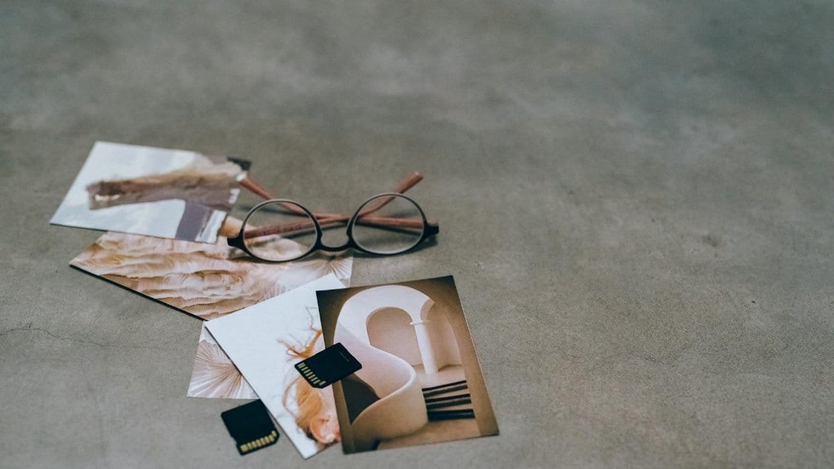 A creative flat lay of eyeglasses, printed photos, and memory cards on a concrete surface.