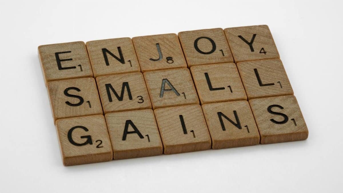 Close-up of Scrabble tiles spelling 'Enjoy Small Gains' on a white surface.