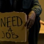 A man holding a cardboard sign reading 'Need a Job', symbolizing unemployment and hardship.