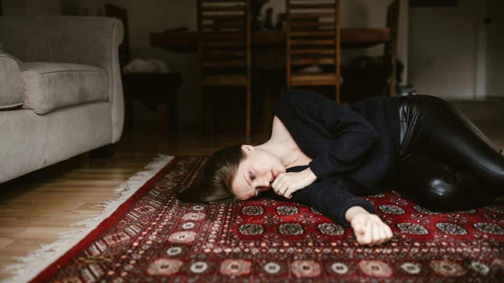 A contemplative woman resting on an intricate oriental rug in a cozy living space.
