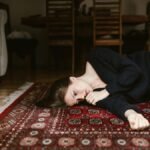 A contemplative woman resting on an intricate oriental rug in a cozy living space.