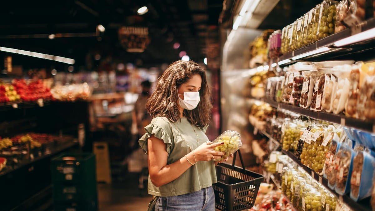 A woman wearing a mask shops for fresh fruits in a grocery store aisle.