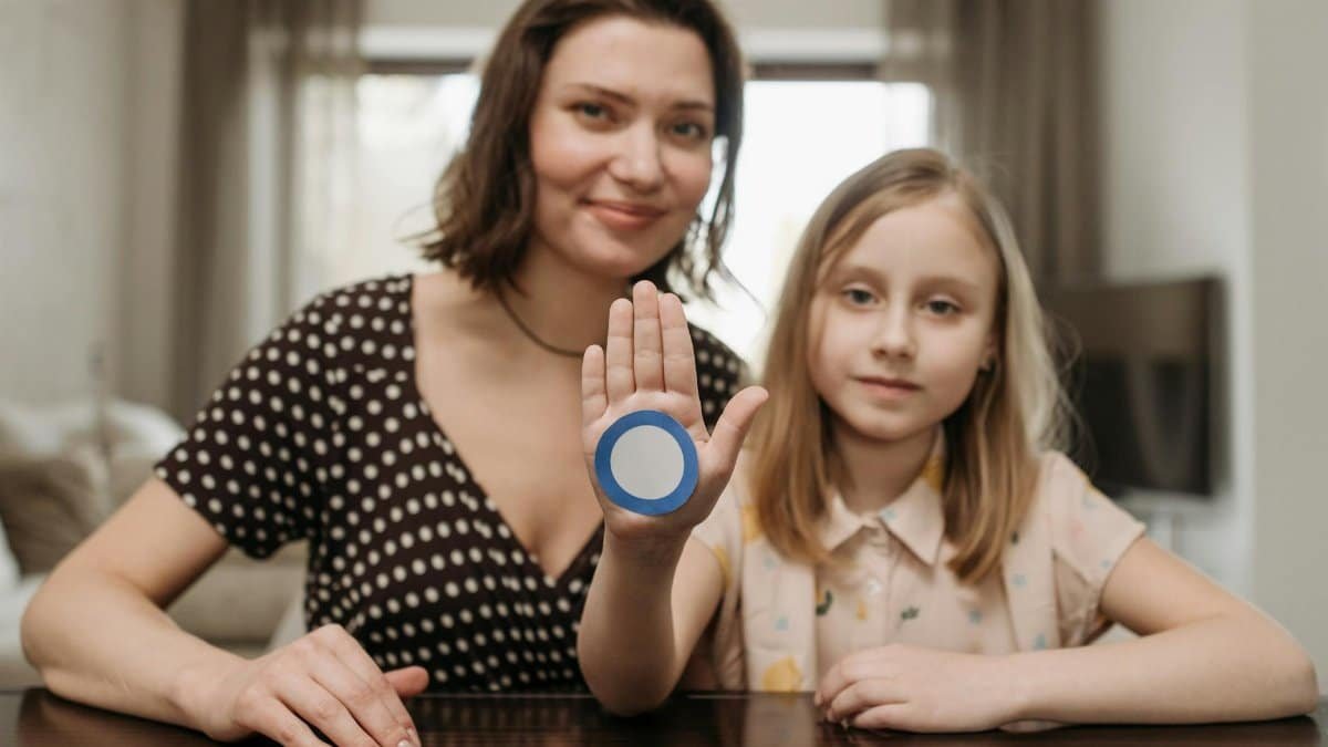 A mother and daughter raise awareness for diabetes with a blue circle symbol indoors.