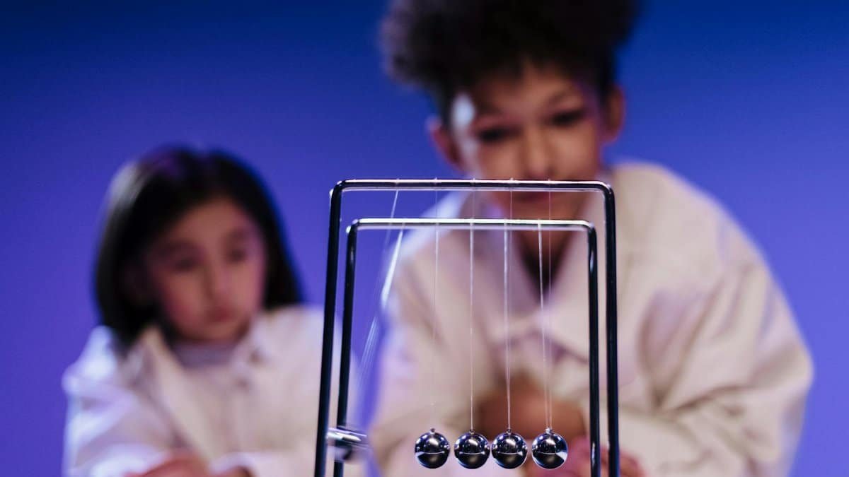 Two children curiously observing a Newton's Cradle in a science setting.