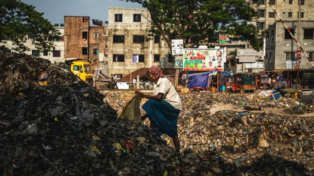 A worker sorting through urban waste in a landfill with buildings in the background.
