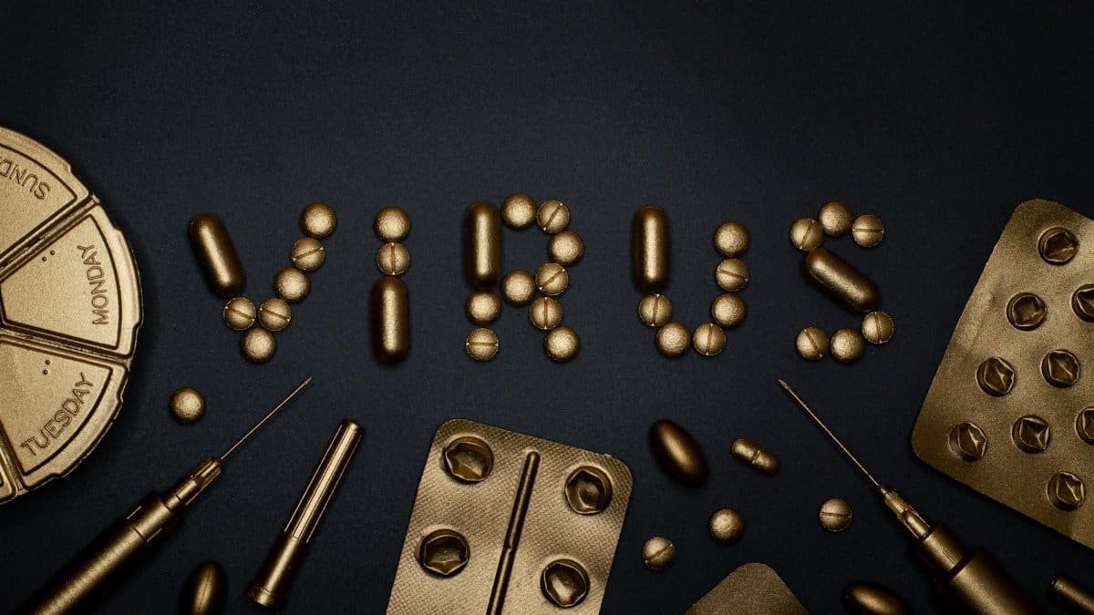 Conceptual image featuring gold pills and syringes forming the word 'virus' on a dark backdrop.