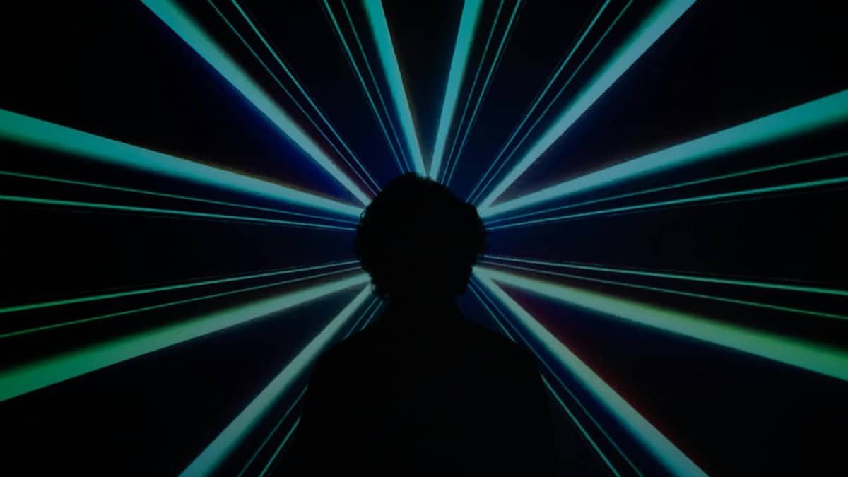 Silhouette of a person in front of a dynamic and colorful laser light display.