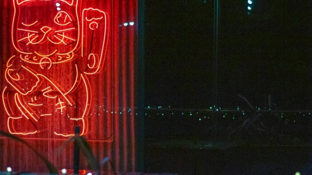 A bright neon sign of a lucky cat, glowing in red during nighttime.