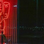 A bright neon sign of a lucky cat, glowing in red during nighttime.