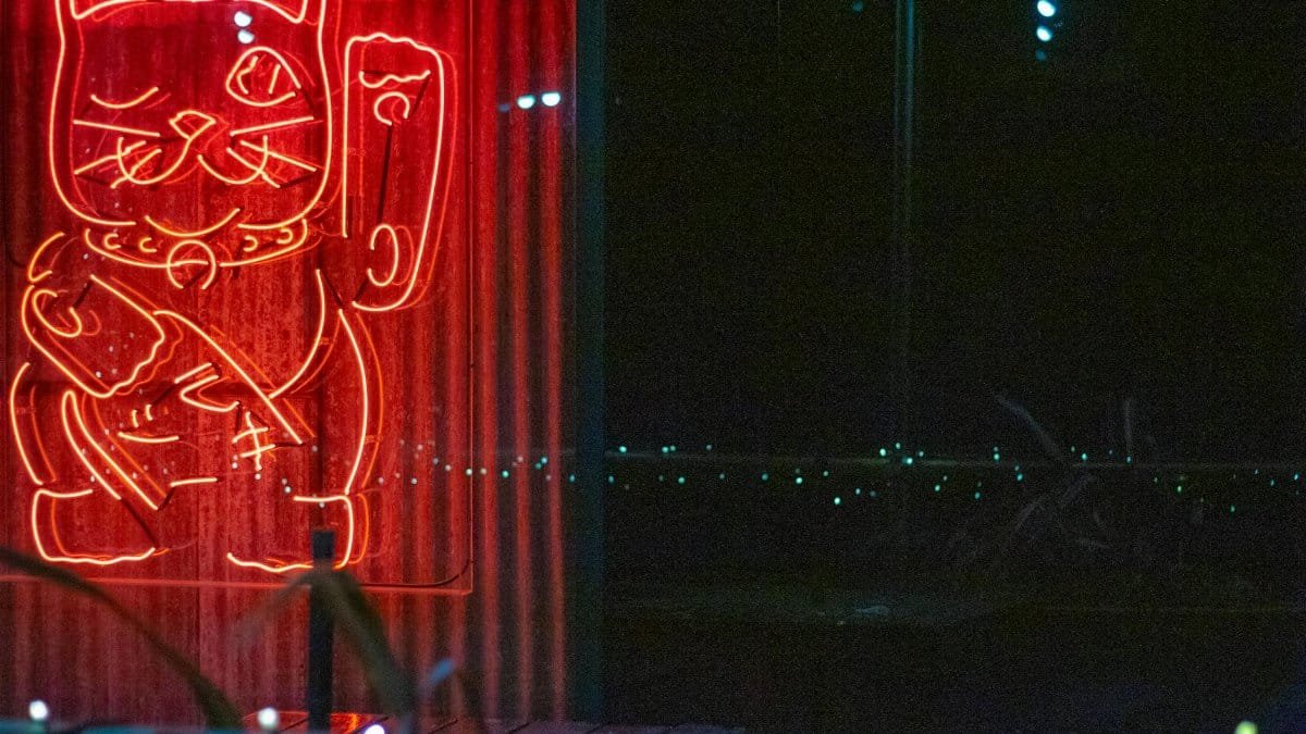 A bright neon sign of a lucky cat, glowing in red during nighttime.