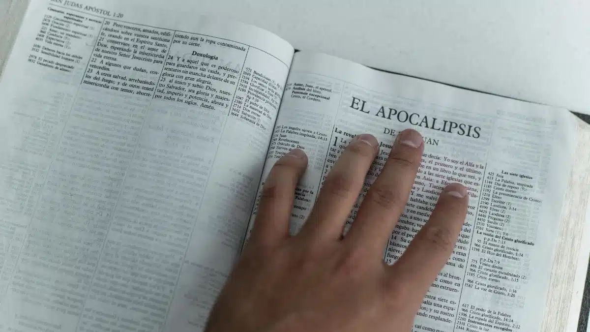 A hand touching Bible pages open to the Book of Revelation, symbolizing faith and study.