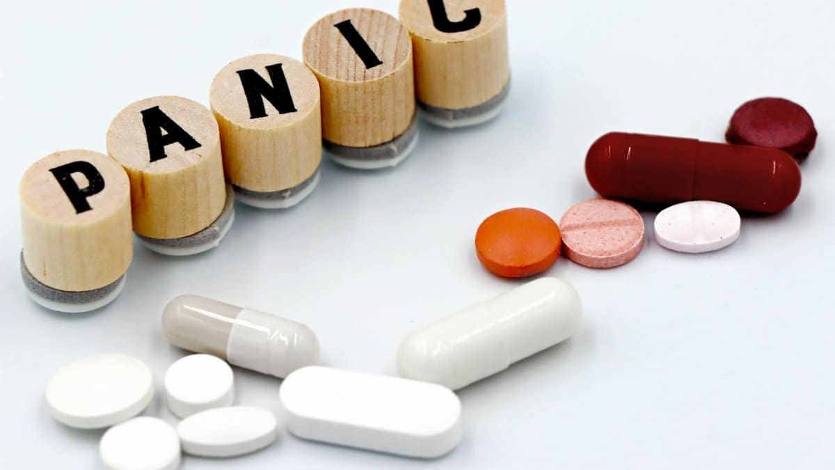 Assorted pills arranged beside wooden tiles spelling 'PANIC', symbolizing anxiety treatment.
