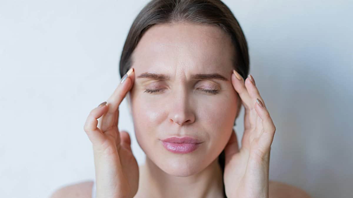Close-up of a woman with closed eyes holding her temples, showing signs of a migraine or headache.