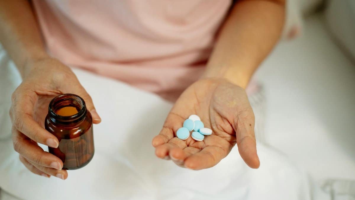 Close-up of an adult taking medication with blue pills in hand, promoting health recovery at home.
