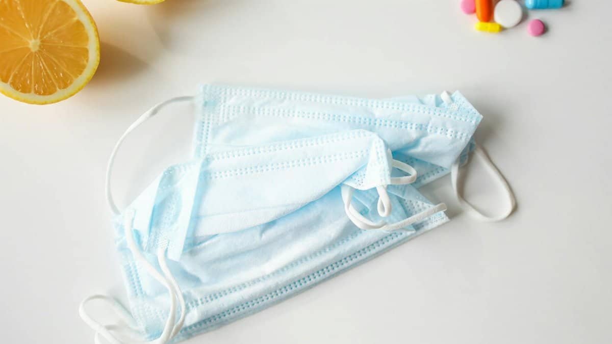 A flat lay of face masks, lemons, and pills on a white surface, emphasizing health and protection.
