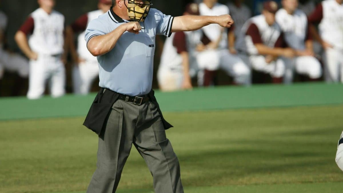 Umpire in action on baseball field with team players in the background.
