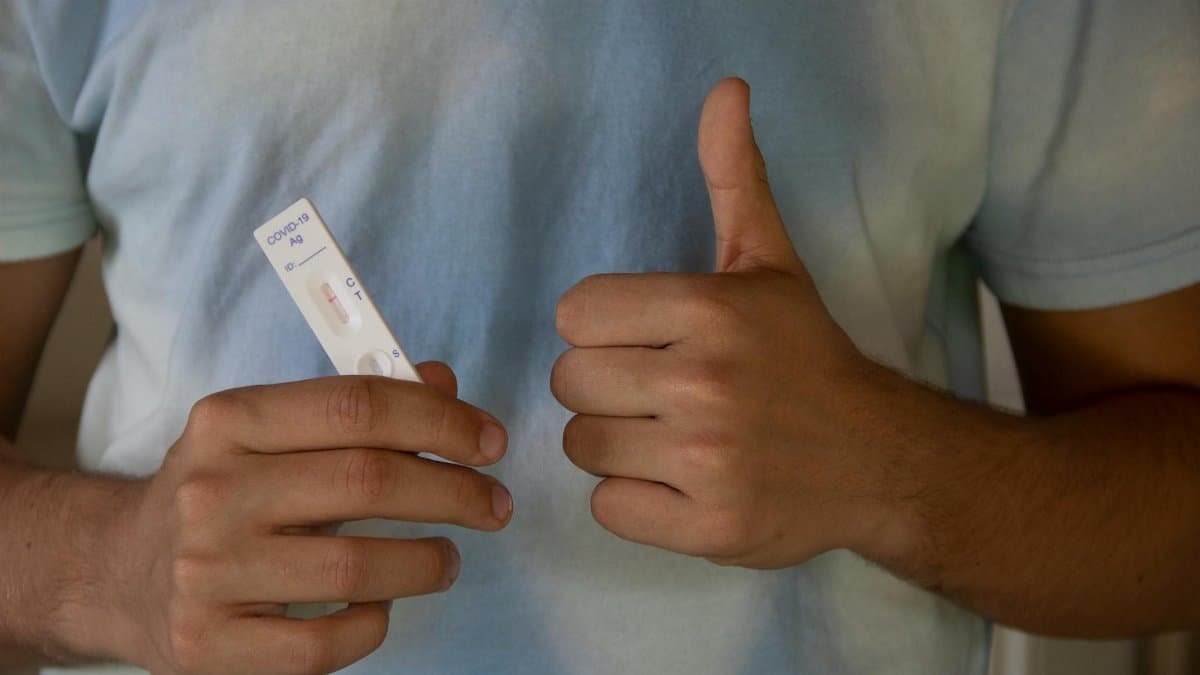 A person showing a COVID-19 antigen test and giving a thumbs up, indicating a negative result.