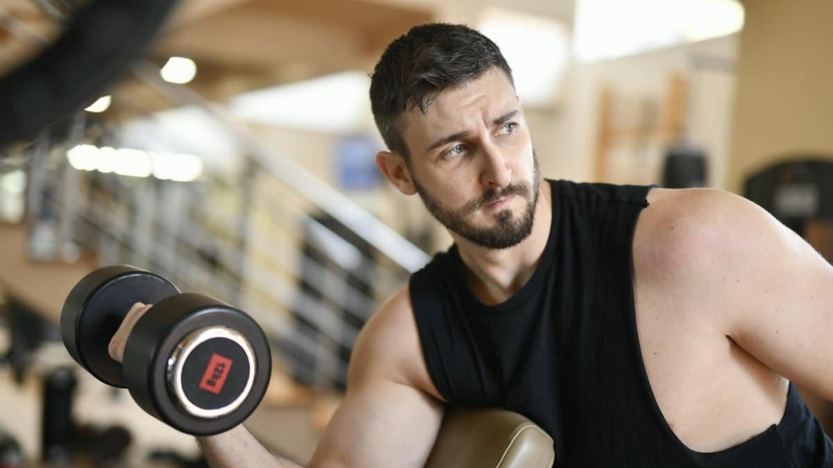 A determined man lifting a dumbbell indoors, showcasing strength and fitness.