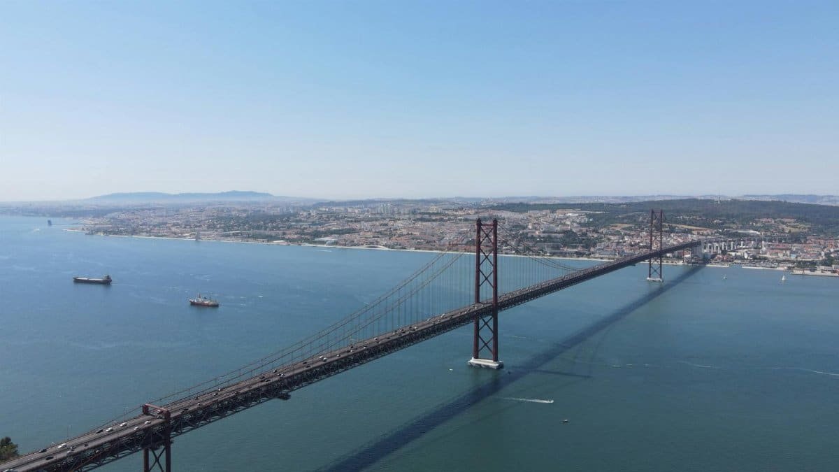 A stunning aerial view of the 25 de Abril Bridge connecting Lisbon across the Tagus River, under a clear blue sky.