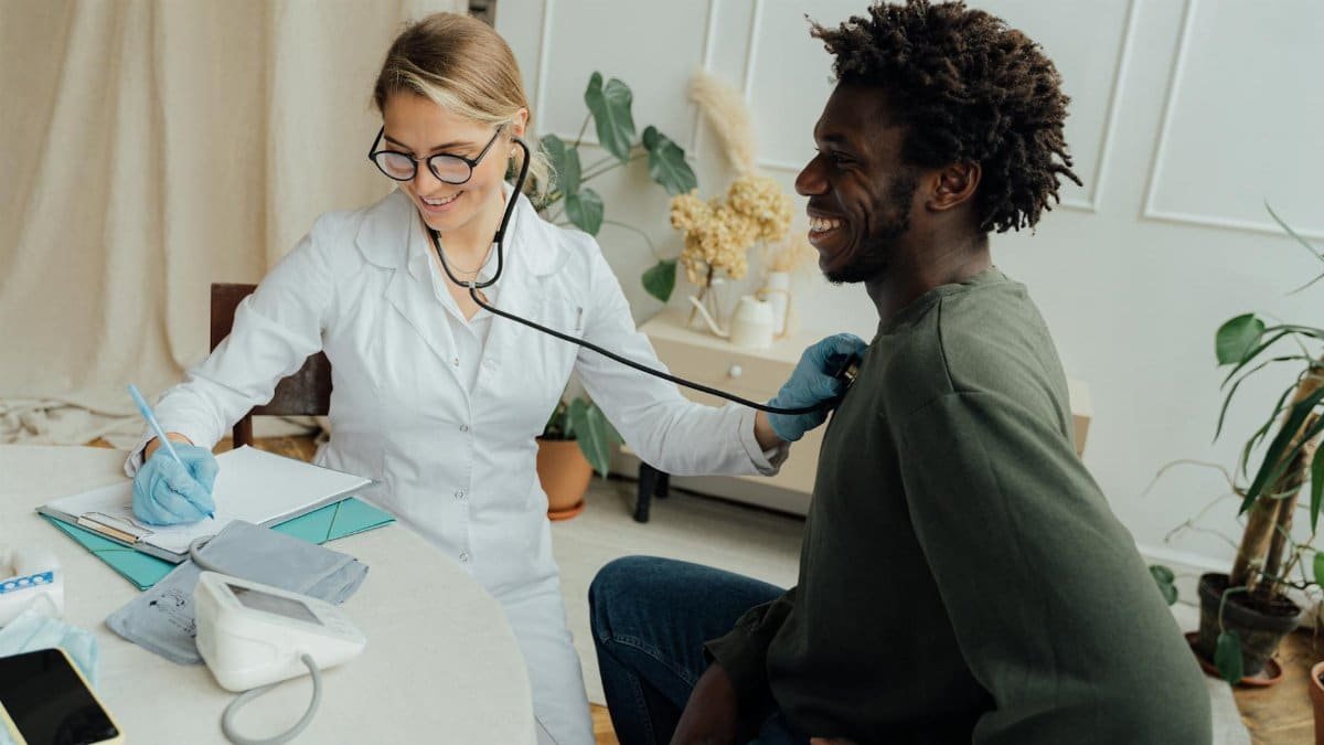Caucasian female doctor checks black male patient's heart rate with stethoscope in a clinic.