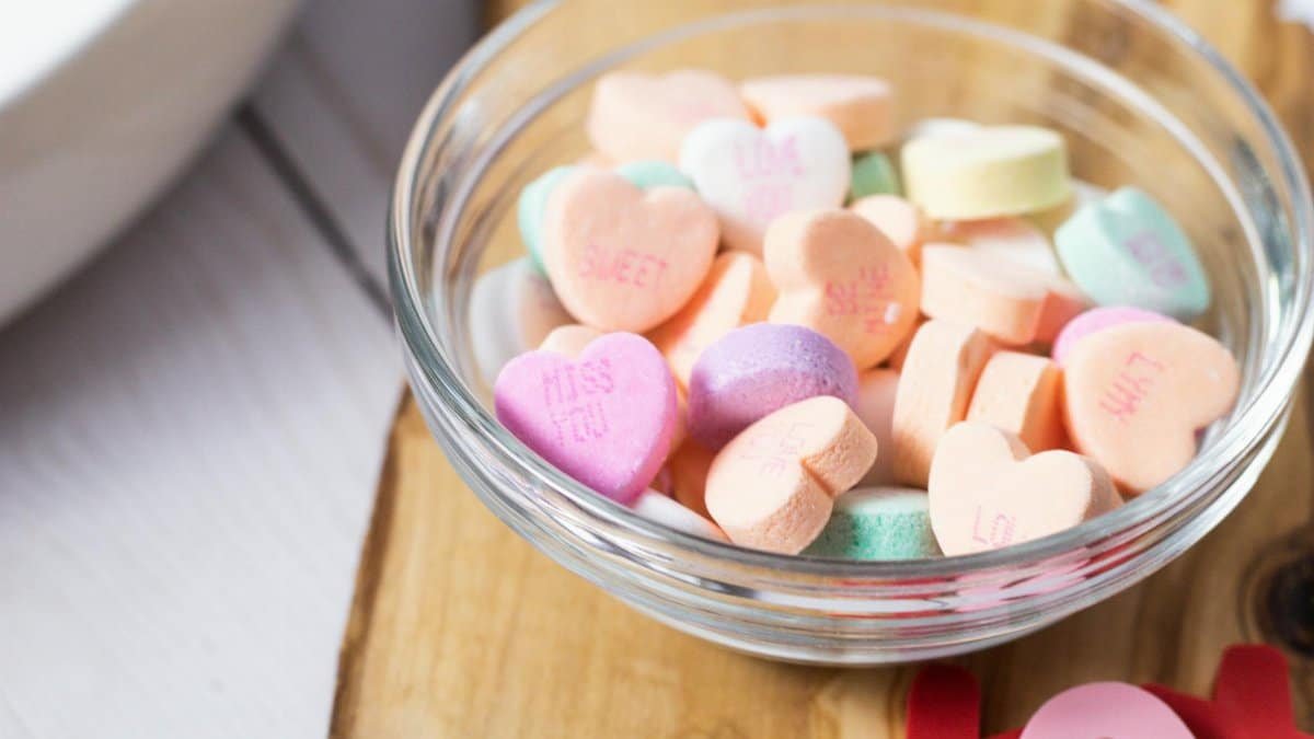 Heart-shaped candies in a glass bowl on wooden surface, perfect for Valentine's.