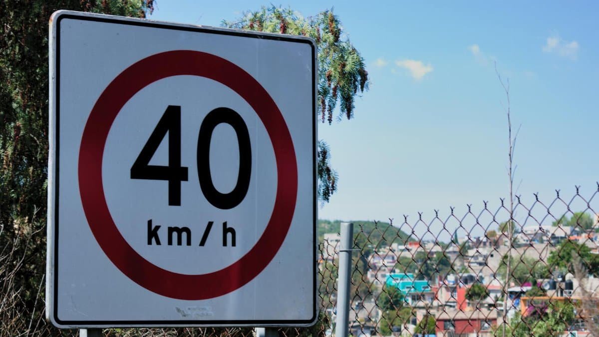 Close-up of a 40 km/h speed limit sign near a chain-link fence and urban landscape.