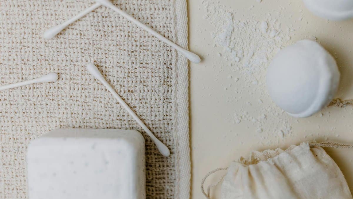 Top view of bath supplies including cotton swabs, soap, and bath bombs on a hemp cloth.