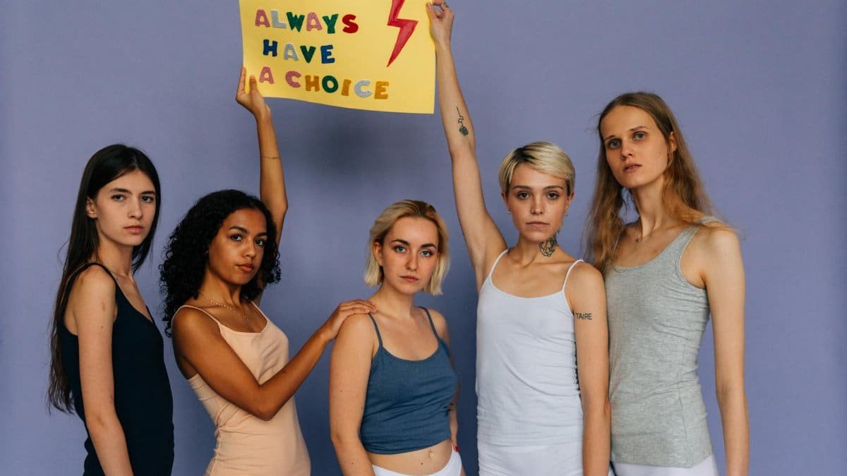 Five women in a studio holding a sign advocating choice, showing empowerment.