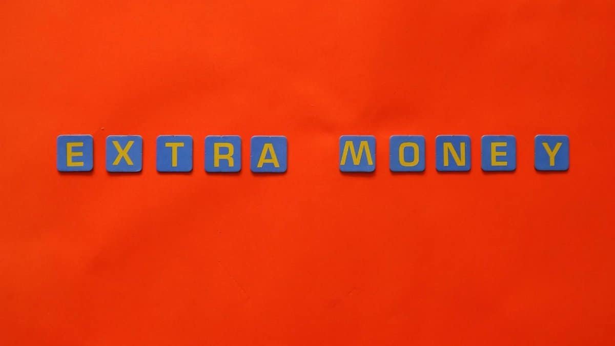 Bright orange background with 'EXTRA MONEY' spelled in blue and yellow tiles, illustrating financial concepts.